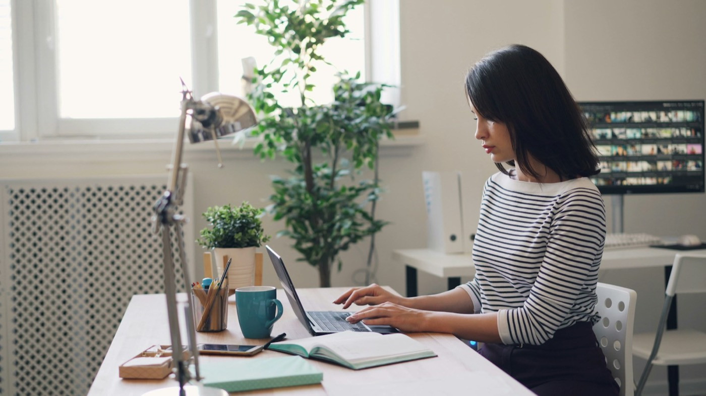 A woman works on a laptop at a tidy desk in a bright office.