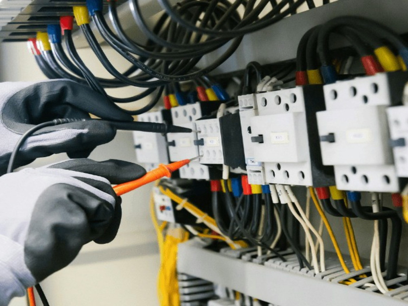 A gloved electrician tests wiring in an electrical panel with a tester.