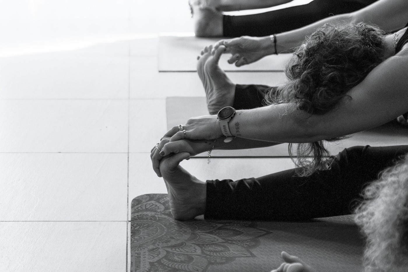 Students in a yoga class stretch forward over their mats, in black and white.